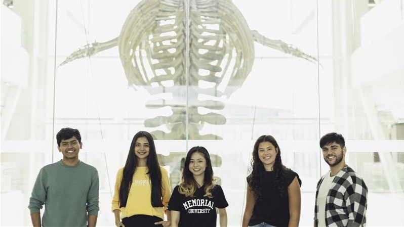Five students stand smiling in front of a large whale skeleton at Memorial University’s Core Science Facility